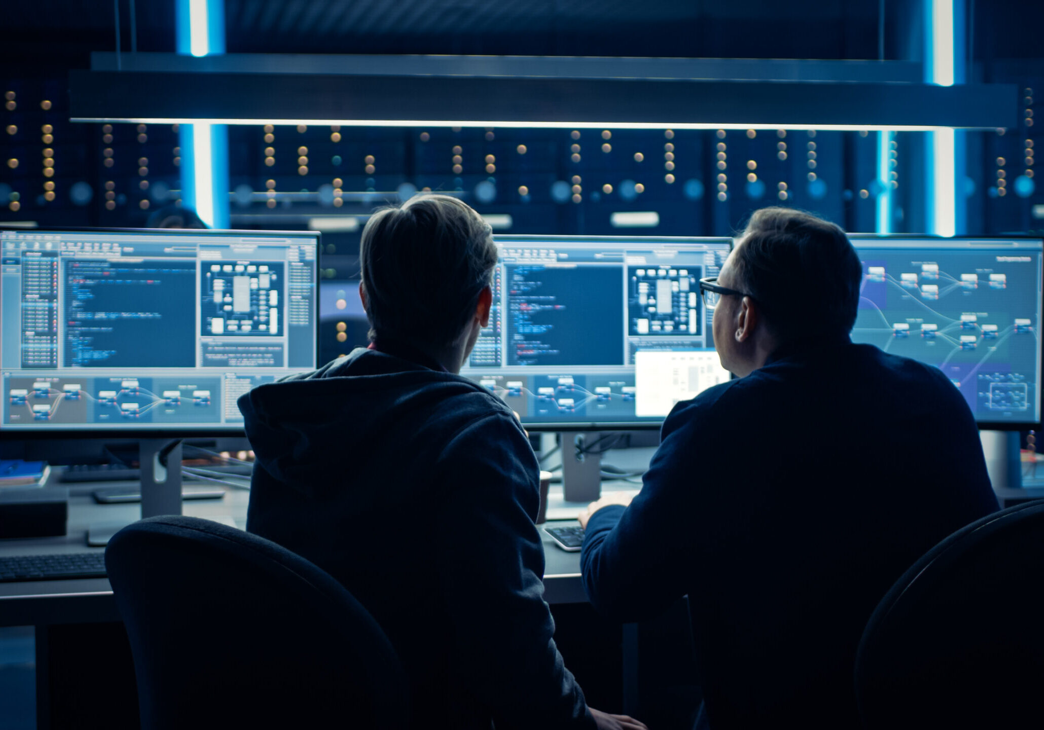 Two Professional IT Programers Discussing Blockchain Data Network Architecture Design and Development Shown on Desktop Computer Display. Working Data Center Technical Department with Server Racks Two Professional IT Programers Discussing Blockchain Data Network Architecture Design and Development Shown on Desktop Computer Display. Working Data Center Technical Department with Server Racks